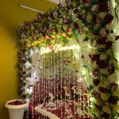 A beautiful 'Welcome Bride' setup with a bed canopy made of flowers and hanging floral strings. A custom neon sign with the couple's names adds a personal and modern touch.