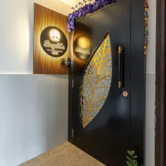 An elegant and artistic entryway, featuring a black door with a golden leaf-patterned jali cutout and a backlit wooden nameplate.