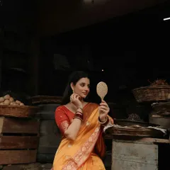 A model in a beautiful yellow and red saree, looking into a traditional mirror. This shot has a vintage, cinematic quality, telling a story of beauty and reflection.