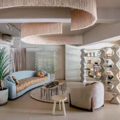 A curated lounge setting within the showroom demonstrates how different textures and forms can coexist harmoniously. The space features a curved blue sofa, sculptural shelving, and a dramatic ceiling installation, all working together to create an immersive and inspiring interior.