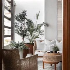 To evoke the airy feel of a traditional Kerala home in a compact apartment, we enlarged the windows and styled the balcony with light rattan furniture, plush white cushions, and abundant greenery.
