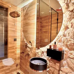 This powder room is all about raw luxury. I contrasted a rough, exposed stone wall with smooth, wood-paneled walls and a sleek, round mirror. The cylindrical pedestal sink and rose gold fixtures add a touch of modern elegance, while the integrated steam bath function makes it a true wellness space.