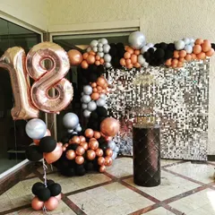 A glamorous 18th birthday celebration featuring a silver sequin wall. The organic balloon garland in rose gold, black, and silver adds a touch of modern sophistication.