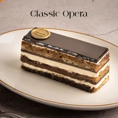 A perfect slice of my Classic Opera pastry. You can see the distinct layers of coffee-soaked almond sponge, rich ganache, and smooth buttercream, all topped with a glossy chocolate glaze.