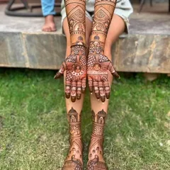 A beautiful outdoor shot showcasing a full bridal mehndi set. The designs on the hands and feet are perfectly matched, featuring architectural elements and traditional patterns.