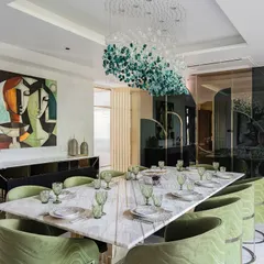 We designed this dining room as a central gathering place for celebration. The long marble dining table is surrounded by bespoke chairs upholstered in a rich green velvet, creating a sense of occasion. Overhead, a sculptural chandelier composed of green and clear glass pieces acts as a floating artwork, tying the entire space together.