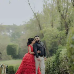 A classic portrait from an engagement shoot in a lush Pune garden. The woman's striking red gown and the couple's confident pose create a timeless and elegant image, showcasing a more formal and styled approach to pre-wedding photography.