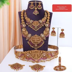 Here is a full bridal set laid out so you can see every beautiful piece. This ruby-studded temple jewellery set includes a choker, haram, vaddanam (waist belt), vanki (armlets), jhumkas, and a maang tikka.