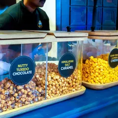 A gourmet popcorn station offering a variety of delicious flavors, including Nutty Tuxedo Chocolate, Himalayan Salt Caramel, and Sour Cream & Onion Cheese.