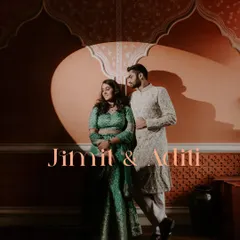 A beautifully lit portrait of a couple against a terracotta-colored wall with traditional Indian arch designs, using a spotlight effect to create a dramatic and intimate feel.