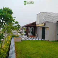 A sprawling terrace garden in New Friends Colony, featuring a lush lawn, extensive planting, and a wooden cottage structure.