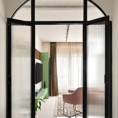 I used a metal and fluted glass partition with a bold arch to create a dramatic entryway into the living room. It separates the space while allowing light to pass through, offering a tantalizing glimpse of the colorful interior.