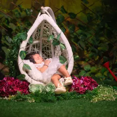A serene image of a newborn sleeping in a white hanging chair, surrounded by lush greenery and flowers, creating a magical garden scene.