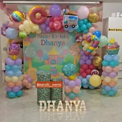 A sweet Candyland theme for Dhanya's birthday. The decor features a pastel-colored balloon arch, large donut and ice cream foil balloons, and light-up marquee letters.