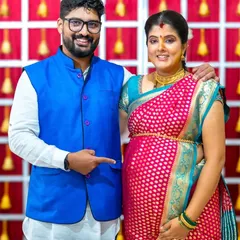 Here they are, posing for a classic baby shower portrait. The proud father to be points happily at the baby bump, while the mother to be radiates joy in her beautiful pink and blue saree. It's a wonderful memory of celebrating with loved ones.