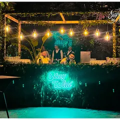 The 'Stay Wild' neon sign was the centerpiece of this jungle-themed bar. I framed the bar with a wooden pergola, hanging Edison bulbs, and dense foliage to create an inviting spot for guests to grab a drink.