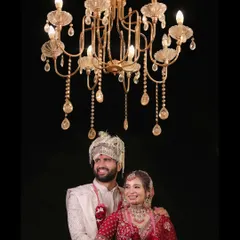 A grand and royal wedding portrait of the couple standing beneath a magnificent crystal chandelier. This shot captures the opulence of the celebration and the couple's regal presence.