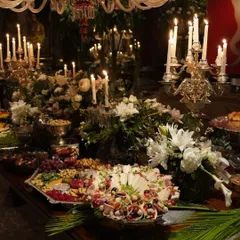 A candlelit grazing table creates an atmosphere of intimate luxury. This setup features an abundant spread of cheeses, cured meats, nuts, and fruits, beautifully arranged amidst glowing candles and elegant white florals for a sophisticated evening event.