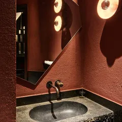 The powder room at Otra, where we used a rich, earthy red plaster on the walls and a hand-carved stone sink. The custom mirror and bespoke light fixtures add to the moody, dramatic atmosphere of the space.