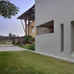 A view of the Tree House from the lawn, showing the relationship between the solid architectural forms and the open green space. The strategic placement of windows and openings in the facade frames views of the landscape while maintaining a sense of privacy.