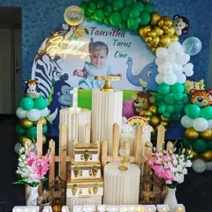 A wild first birthday with a jungle theme. This decoration includes a green and gold balloon arch, animal character cutouts, a personalized backdrop, and a cute picket fence for a complete look.