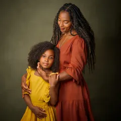 A mother's gentle touch and loving gaze toward her daughter. This portrait captures the tender, protective bond between them. The rich colors of their dresses against the painterly green background create a warm and vibrant image of family love.