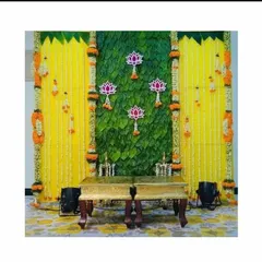 A beautiful backdrop for a Varamahalakshmi festival, featuring a banana leaf panel, yellow flower curtains, and hanging lotus motifs.