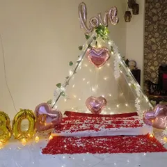 An intimate cabana setup for a 30th birthday, with a bed of rose petals, heart-shaped balloons, and fairy lights.