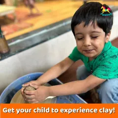 A toddler gets to experience the feel of clay on the potter's wheel for the first time, with a parent's reassuring presence nearby.