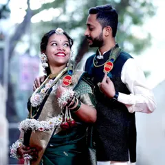 A happy couple shares a candid moment during their outdoor baby shower photoshoot. The mom-to-be is adorned in traditional floral jewelry, and they both wear playful 'Aai' (Mom) and 'Baba' (Dad) badges.