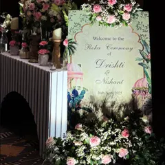 A beautiful welcome for an elegant Roka ceremony. This entrance features a custom welcome sign surrounded by lush arrangements of white and pink roses, setting a sophisticated tone for the event.