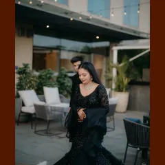 A wide shot capturing the couple at their outdoor reception venue. The elegant black attire and sophisticated setting create a luxurious feel.