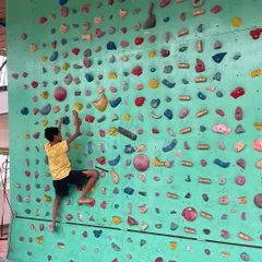 Here, a young climber navigates a bouldering route on our wall. We encourage kids to find their own path, focusing on the process of problem solving and building focus rather than just reaching the top.