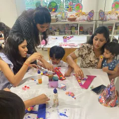 A table full of creativity, with mothers and their children working together on monogram art. It's a joyful, hands-on activity that's perfect for a fun family outing or a kids' party.
