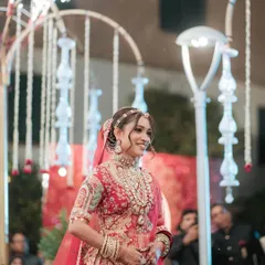 A stunning bride making her grand entrance at her reception. Her hair is styled in a beautiful bun with flowers, perfect for her red lehenga.