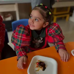 A young girl smiles with delight at her decorated cookie during our Christmas workshop. Holiday-themed activities make learning festive and fun.