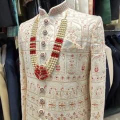 This is extravagance defined. An ivory sherwani featuring dense, fine embroidery in red and gold tones, paired with a multi-layered pearl and ruby necklace for a majestic groom's outfit.