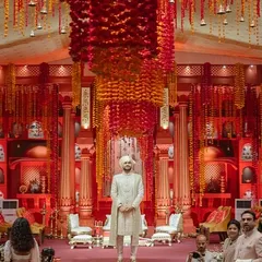 The groom's entrance at the Lal Bagh wedding. The grand scale of the custom-built temple structure, with its towering red pillars and cascading flowers, creates a powerful and unforgettable moment.