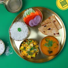 A vibrant and wholesome vegetarian thali plated on traditional brass. It includes our fresh sabzi, dal, rice, salad, and rotis, bringing a taste of home to your lunch break.