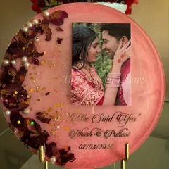 A round decorative plate in a soft pink resin, perfect for preserving engagement flowers. This design features the couple's photo, their names, and the phrase "We Said Yes" to commemorate the special occasion. The preserved petals are arranged in a crescent shape, accented with pearls and gold flakes.