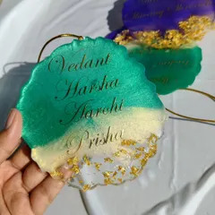 A custom car hanging made for a family, featuring four names in elegant gold script. The design uses a blend of green and clear resin with gold foil for a luxurious feel.