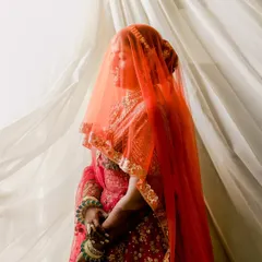 The veil shot is always so magical. The sheer orange dupatta adds a soft, ethereal glow, highlighting the bride's happiness. This is a moment of quiet reflection before the ceremonies begin.