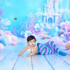 A beautiful shot of a baby in a mermaid costume, crawling on a set designed to look like the ocean floor. The underwater castle and coral create a perfect fantasy world.
