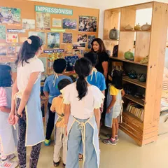An instructor gathers students to discuss the Impressionist movement, using visual aids and examples to explain the concepts of light and color before they begin their Van Gogh inspired paintings.