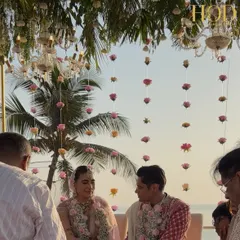A candid moment of the couple during their seaside ceremony, with hanging rose strings and palm trees framing the beautiful ocean view.