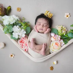 A beautiful overhead shot of a newborn sleeping peacefully in a fabric hammock, adorned with a tiny crown and surrounded by flowers. This pose is perfect for capturing their delicate features in a creative way.