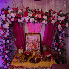 A floral arch made of red and white roses for a home pooja or 'jagran'. The setup provides a beautiful frame for the deity's picture and creates a sacred ambiance.