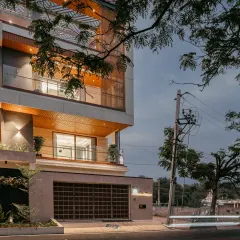 Another evening perspective of the Hennur residence, capturing the light trails and the home's relationship with its surroundings. The lit balconies and soffits add depth and dimension to the contemporary facade.