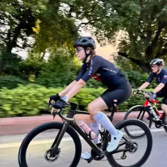 A female cyclist in full gear, focused on the road ahead during a group training ride. Her confident posture shows the strength and skill our members develop.