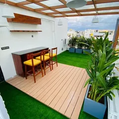 We transformed this rooftop terrace into a chic entertainment zone, complete with a custom bar, WPC wood-look decking, and integrated planters. The glass-topped pergola and modern pendant lighting make it a functional and stylish space, day or night.